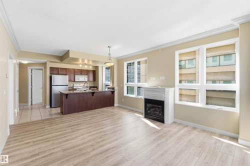 Open-concept living area featuring wood-finish flooring, a contemporary fireplace with a white mantel, and multiple windows - #708 9939 109 St Nw, Edmonton, AB - Indoor With Fireplace