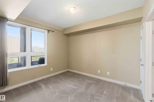 Spacious room featuring broad windows with city surroundings, crown molding, and neutral-toned carpeting - #708 9939 109 St Nw, Edmonton, AB - Indoor Photo Showing Other Room