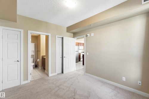 Neutral-toned room featuring light-colored carpeting, multiple paneled doors, and direct access to a bathroom with tile flooring and a vanity - #708 9939 109 St Nw, Edmonton, AB - Indoor Photo Showing Other Room