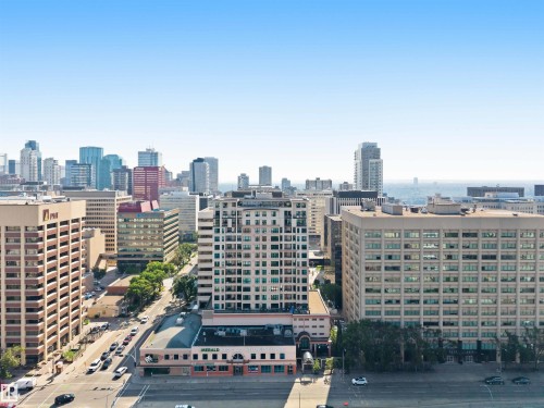Panoramic cityscape featuring diverse architectural styles, visible roadways with vehicles, multiple high-rise structures, and a distant body of water - #708 9939 109 St Nw, Edmonton, AB - Outdoor With View
