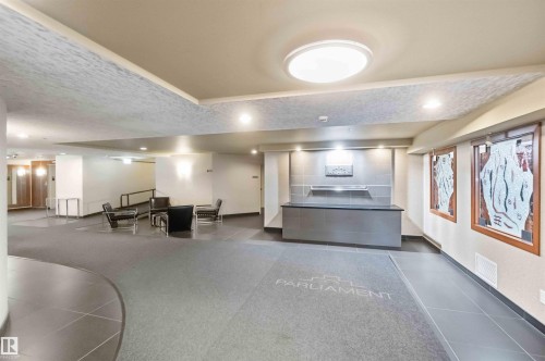 Spacious lobby area featuring large format floor tiling, a recessed ceiling with flush-mounted lighting, a reception desk with tile backdrop, and decorative framed wall art - #708 9939 109 St Nw, Edmonton, AB - Indoor Photo Showing Other Room