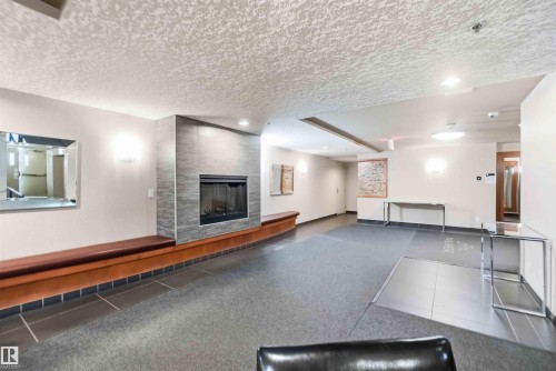 Entryway featuring a tiled fireplace with a built-in hearth and seating, wall sconces, ceiling lighting, and a textured ceiling - #708 9939 109 St Nw, Edmonton, AB - Indoor With Fireplace