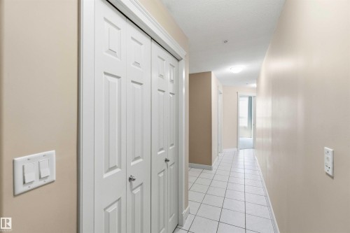 Hallway featuring white panel bi-fold doors, light tile flooring, and neutral wall paint - #708 9939 109 St Nw, Edmonton, AB - Indoor Photo Showing Other Room