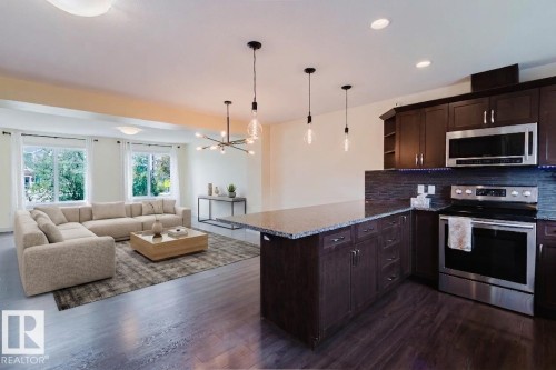 Open-concept living space featuring wood-finish flooring, a kitchen island with stone countertop, dark wood cabinetry, stainless steel appliances, and multiple windows - 6717 Elston Lane Nw, Edmonton, AB - Indoor