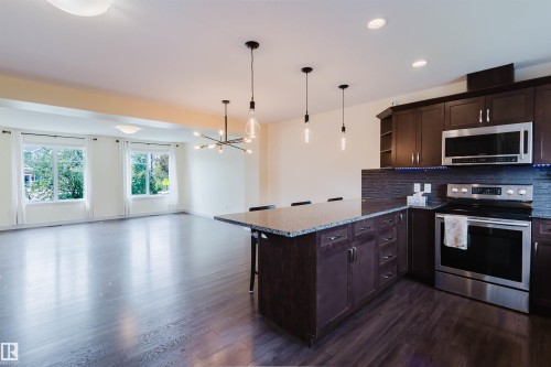 Kitchen featuring dark wood cabinetry, stainless steel appliances, a granite countertop island with seating, and pendant lighting - 6717 Elston Lane Nw, Edmonton, AB - Indoor Photo Showing Kitchen