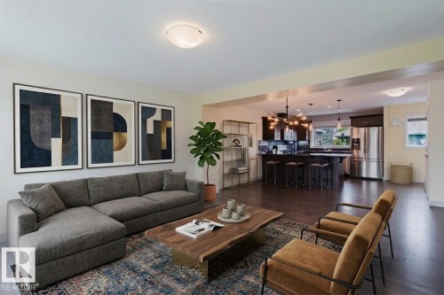 Open-concept living space featuring wood-finish flooring, recessed lighting, and a kitchen with dark cabinetry, stainless steel refrigerator, and a central island with pendant lighting - 6717 Elston Lane Nw, Edmonton, AB - Indoor Photo Showing Living Room