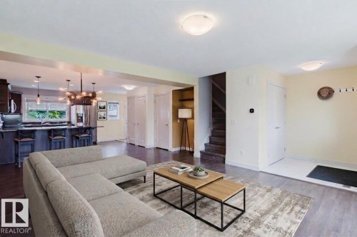 Open-concept living area featuring a kitchen with dark cabinetry, stainless steel appliances, and a central island with bar seating - 6717 Elston Lane Nw, Edmonton, AB - Indoor Photo Showing Living Room