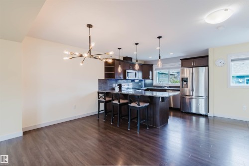 Open-concept kitchen and dining area featuring dark wood-finish flooring, a contemporary sputnik chandelier, and a kitchen island with seating - 6717 Elston Lane Nw, Edmonton, AB - Indoor Photo Showing Other Room