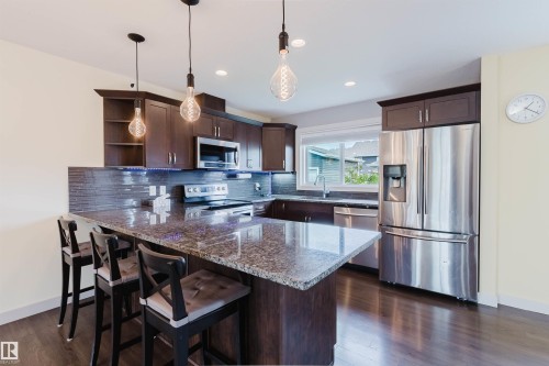 Kitchen featuring dark wood-finish cabinetry, granite countertops, stainless steel appliances, and wood-finish flooring - 6717 Elston Lane Nw, Edmonton, AB - Indoor Photo Showing Kitchen With Stainless Steel Kitchen With Double Sink