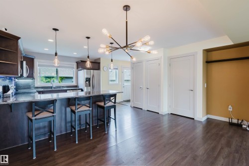 Open-concept kitchen and living area featuring dark wood-finish flooring, a kitchen island with seating, dark cabinetry, and stainless steel appliances - 6717 Elston Lane Nw, Edmonton, AB - Indoor Photo Showing Kitchen With Upgraded Kitchen