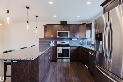 Open-concept kitchen featuring dark wood cabinetry, stainless steel appliances, and a grey tile backsplash - 6717 Elston Lane Nw, Edmonton, AB - Indoor Photo Showing Kitchen With Stainless Steel Kitchen With Upgraded Kitchen