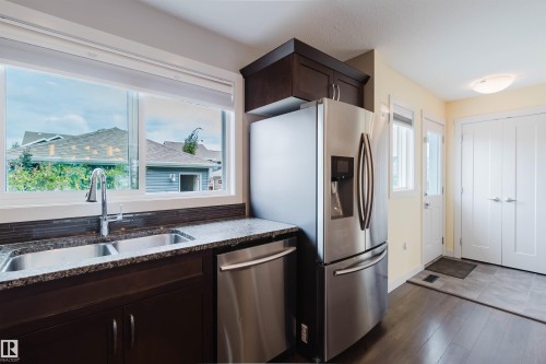 Kitchen featuring a double basin stainless steel sink, stainless steel appliances, dark wood-finish cabinetry, and a granite-style countertop - 6717 Elston Lane Nw, Edmonton, AB - Indoor Photo Showing Kitchen With Double Sink