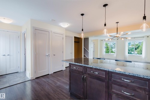Kitchen island featuring dark wood cabinetry, stainless steel hardware, and a speckled stone countertop - 6717 Elston Lane Nw, Edmonton, AB - Indoor