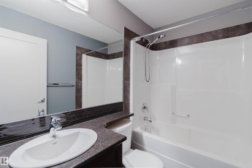 Bathroom featuring a tub/shower combination with a shower wand, a vanity with a drop-in sink, a wall-mounted mirror, and dark tile accents - 6717 Elston Lane Nw, Edmonton, AB - Indoor Photo Showing Bathroom