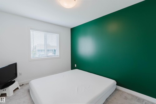 Interior room featuring a prominent green accent wall, white painted walls, and a window with white blinds - 6717 Elston Lane Nw, Edmonton, AB - Indoor Photo Showing Bedroom