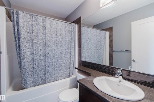 Bathroom featuring a white built-in tub and shower combination, a dark countertop vanity with an oval sink, a mosaic tile backsplash, and a large wall-mounted mirror - 6717 Elston Lane Nw, Edmonton, AB - Indoor Photo Showing Bathroom