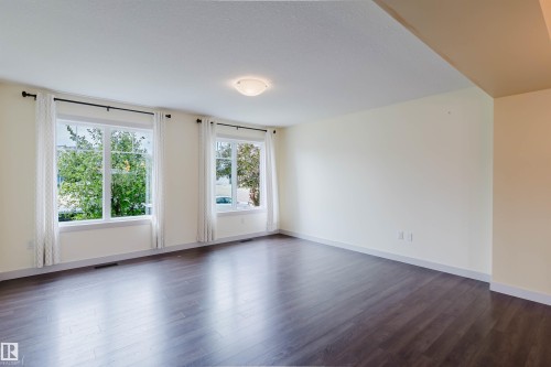 Spacious interior room featuring dark wood-finish flooring, two large windows with white trim, and a semi-flush mount ceiling light fixture - 6717 Elston Lane Nw, Edmonton, AB - Indoor