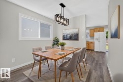 Bright dining area with wood-finish flooring, a contemporary black metal chandelier, light gray walls, and a white-trimmed window - 