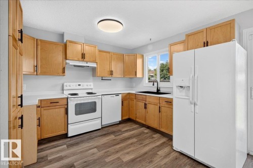 Kitchen featuring wood-finish cabinetry, white countertops, a white appliance suite, a black basin sink with a matte black faucet, and wood-finish flooring - 4212 32 Avenue Nw, Edmonton, AB - Indoor Photo Showing Kitchen