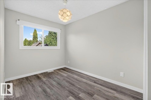 Neutral-toned room featuring a large window, contemporary ceiling light fixture, wood-finish flooring, and white baseboards - 4212 32 Avenue Nw, Edmonton, AB - Indoor Photo Showing Other Room
