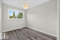 Neutral-toned room featuring a large window, contemporary ceiling light fixture, wood-finish flooring, and white baseboards - 