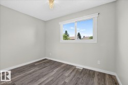 Room featuring light gray walls, wood-finish flooring, a white trim window, and a ceiling-mounted light fixture - 