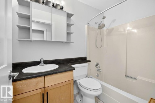 Full bathroom featuring a light wood-finish vanity with dark countertop, an oval undermount sink, a shower-tub combination with a curved shower rod, and a mirrored medicine cabinet with integrated shelving - 4212 32 Avenue Nw, Edmonton, AB - Indoor Photo Showing Bathroom