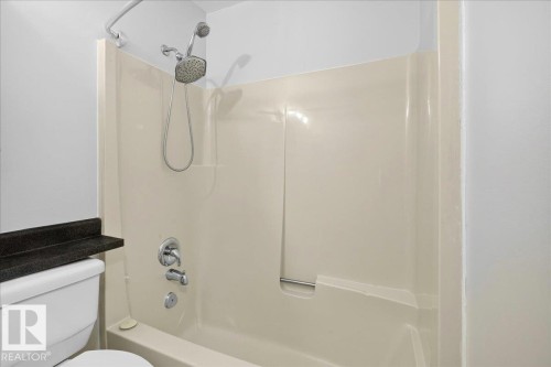 Tub and shower combination featuring a multi-function showerhead with a handheld sprayer, chrome fixtures, and a light-colored tub surround - 4212 32 Avenue Nw, Edmonton, AB - Indoor Photo Showing Bathroom