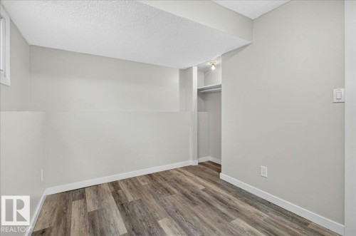 Room featuring wood-finish flooring, light gray walls, white trim, and a built-in closet with shelving and a hanging rod - 4212 32 Avenue Nw, Edmonton, AB - Indoor