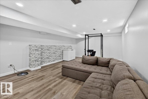 Spacious lower-level room featuring wood-finish flooring, recessed lighting, and a white brick accent wall - 4212 32 Avenue Nw, Edmonton, AB - Indoor