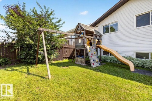 Expansive backyard featuring a wood-tone privacy fence, mature landscaping, and a multi-level play structure with a rock wall and slide - 4212 32 Avenue Nw, Edmonton, AB - Outdoor