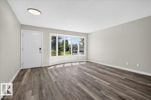 Spacious room featuring wood-finish flooring, a contemporary ceiling light fixture, a paneled entry door with smart lock, and a large bay window - 4212 32 Avenue Nw, Edmonton, AB - Indoor