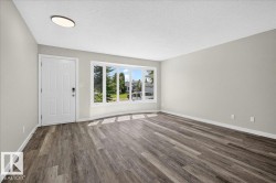 Spacious room featuring wood-finish flooring, a contemporary ceiling light fixture, a paneled entry door with smart lock, and a large bay window - 