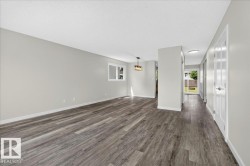 Open concept living space featuring wood-finish flooring, neutral paint, a contemporary chandelier, and a hallway leading to a sliding glass door - 