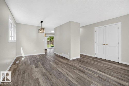 Spacious interior with wood-finish flooring, light grey walls, white trim, and a contemporary linear chandelier - 4212 32 Avenue Nw, Edmonton, AB - Indoor Photo Showing Other Room