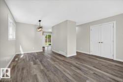 Spacious interior with wood-finish flooring, light grey walls, white trim, and a contemporary linear chandelier - 
