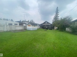 Expansive green lawn with a wood fence, a light blue and white storage shed, and a raised garden bed - 