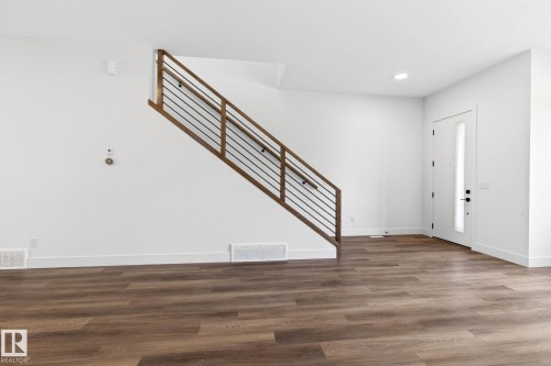 Entryway featuring wood-finish flooring, a contemporary staircase with wood and metal railing, a white entry door with frosted glass insert, recessed lighting, and white baseboards - 5308 103A Avenue, Edmonton, AB - Indoor Photo Showing Other Room