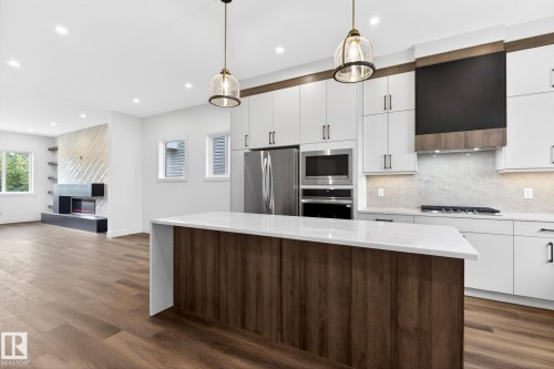 Contemporary kitchen featuring white cabinetry, stainless steel appliances, a center island with a light-toned countertop, and wood-finish flooring - 5308 103A Avenue, Edmonton, AB - Indoor Photo Showing Kitchen With Upgraded Kitchen