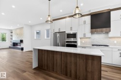 Contemporary kitchen featuring white cabinetry, stainless steel appliances, a center island with a light-toned countertop, and wood-finish flooring - 