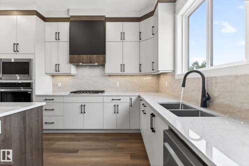 Contemporary kitchen featuring white cabinetry with dark hardware, light-toned stone backsplash, and wood-finish flooring - 5308 103A Avenue, Edmonton, AB - Indoor Photo Showing Kitchen With Double Sink With Upgraded Kitchen
