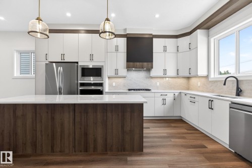 Contemporary kitchen featuring a large central island with wood-finish paneling, white cabinetry, stainless steel appliances, and a light-toned backsplash - 5308 103A Avenue, Edmonton, AB - Indoor Photo Showing Kitchen With Upgraded Kitchen