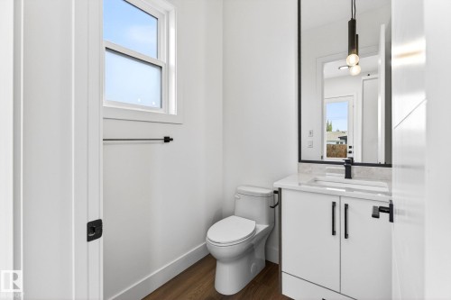 Modern powder room featuring a white vanity with a stone countertop, a black-framed mirror, contemporary pendant lighting, wood-finish flooring, and a window with natural light - 5308 103A Avenue, Edmonton, AB - Indoor Photo Showing Bathroom