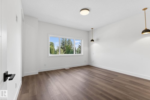 Spacious room featuring wood-finish flooring, white walls, and a large window with exterior tree scenery - 5308 103A Avenue, Edmonton, AB - Indoor Photo Showing Other Room