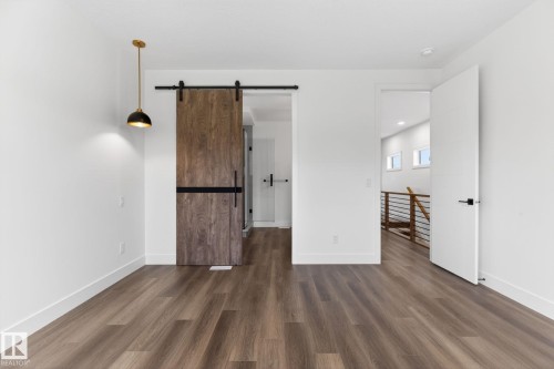Spacious room featuring wood-finish flooring, a modern barn door with black hardware, a contemporary pendant light fixture, and white trim - 5308 103A Avenue, Edmonton, AB - Indoor Photo Showing Other Room