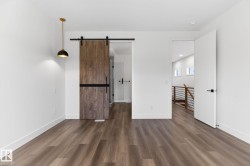 Spacious room featuring wood-finish flooring, a modern barn door with black hardware, a contemporary pendant light fixture, and white trim - 