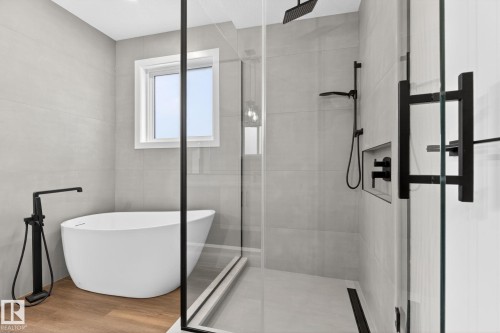 Freestanding soaking tub with floor-mounted matte black faucet, walk-in shower with matte black hardware, tiled shower walls, and a recessed shower niche - 5308 103A Avenue, Edmonton, AB - Indoor Photo Showing Bathroom