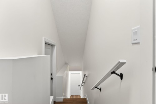 Staircase featuring wood-finish flooring, white walls, and a contemporary white handrail with black brackets - 5308 103A Avenue, Edmonton, AB - Indoor Photo Showing Other Room