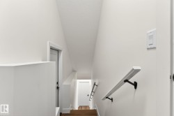 Staircase featuring wood-finish flooring, white walls, and a contemporary white handrail with black brackets - 