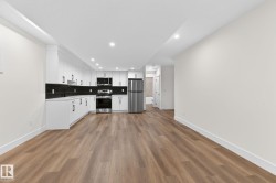 Open-concept living area featuring wood-finish flooring, recessed lighting, and a kitchen with white cabinetry, stainless steel appliances, and a black tile backsplash - 